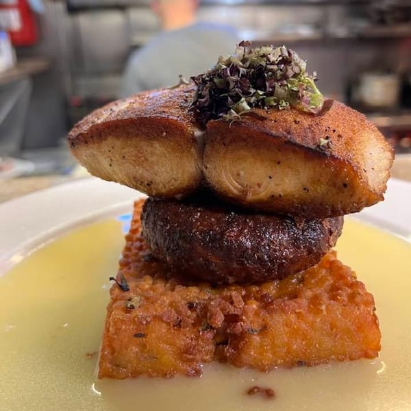 Seared scallops with dark brown crust, topped with herbs, on a bed of crispy polenta in sauce.