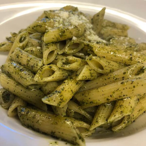 Penne pasta with pesto sauce and grated cheese in a white bowl at Marinelli's Pizza.