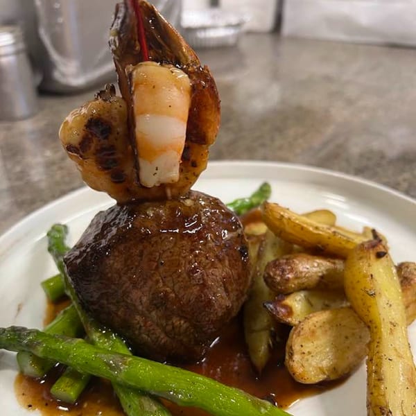 Steak with shrimp skewer, roasted potatoes, and asparagus on a white plate.