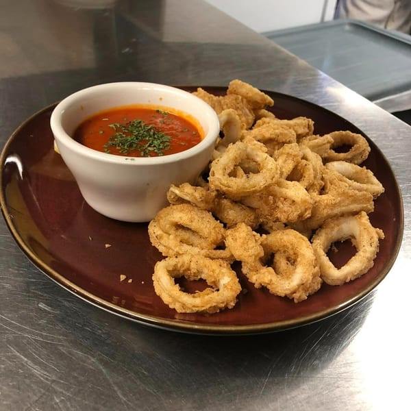 Crispy fried calamari rings with a side of Marinelli's red dipping sauce, garnished with parsley.