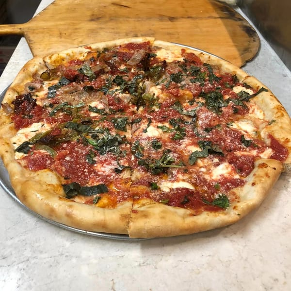 A Marinelli's Pizza with red sauce, mozzarella, fresh basil, and sausage on a metal pan.