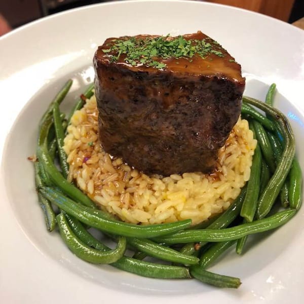 Braised short rib with gravy, rice pilaf, and green beans on a white plate.